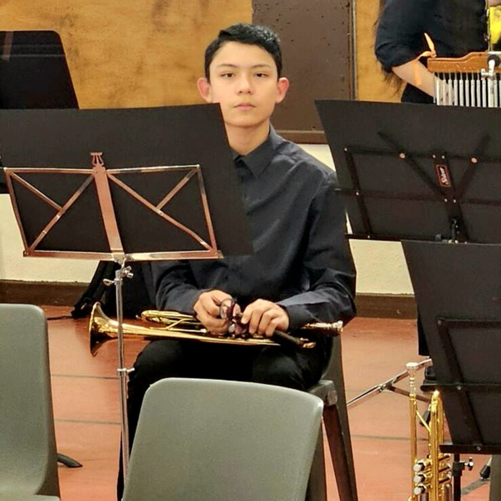 Portrait de Jérémie Rios avec sa trompette, il est assis sur une chaise. derrière un lutrin sur une scène au sein d'un orchestre