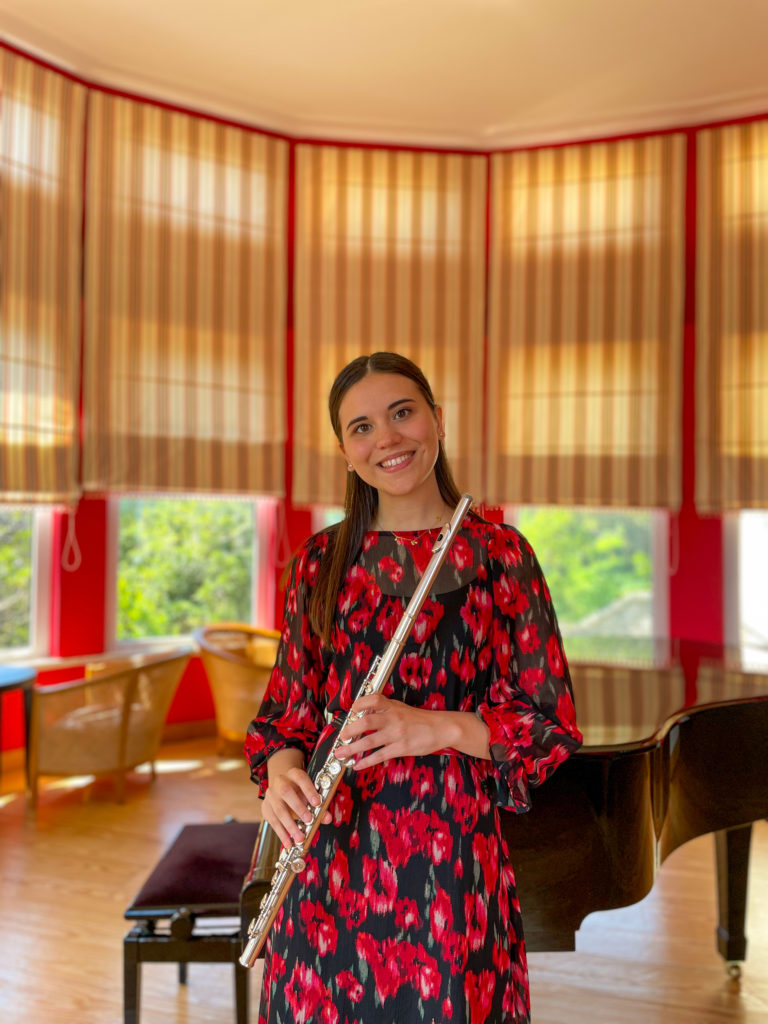 Portrait d'Helena Silva avec sa flûte traversière se tenant devant un piano.